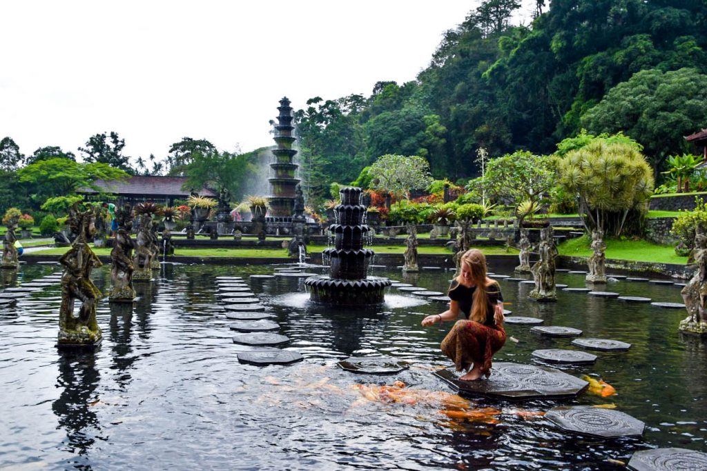 Ellen feeding some fish while sitting on the stepping stones of the Tirta Gangga Temple pond.