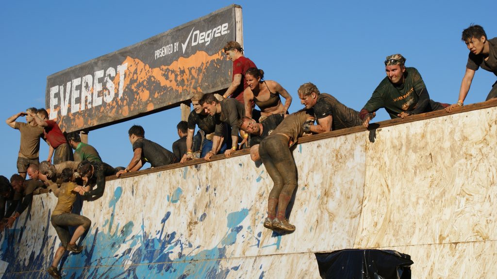 Participants helping each other climb a wall during a Tough Mudder obstacle challenge