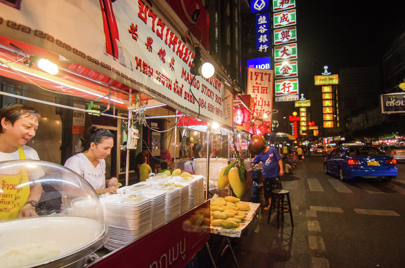 Street food vendors serving food along a brightly lit Bangkok street at night