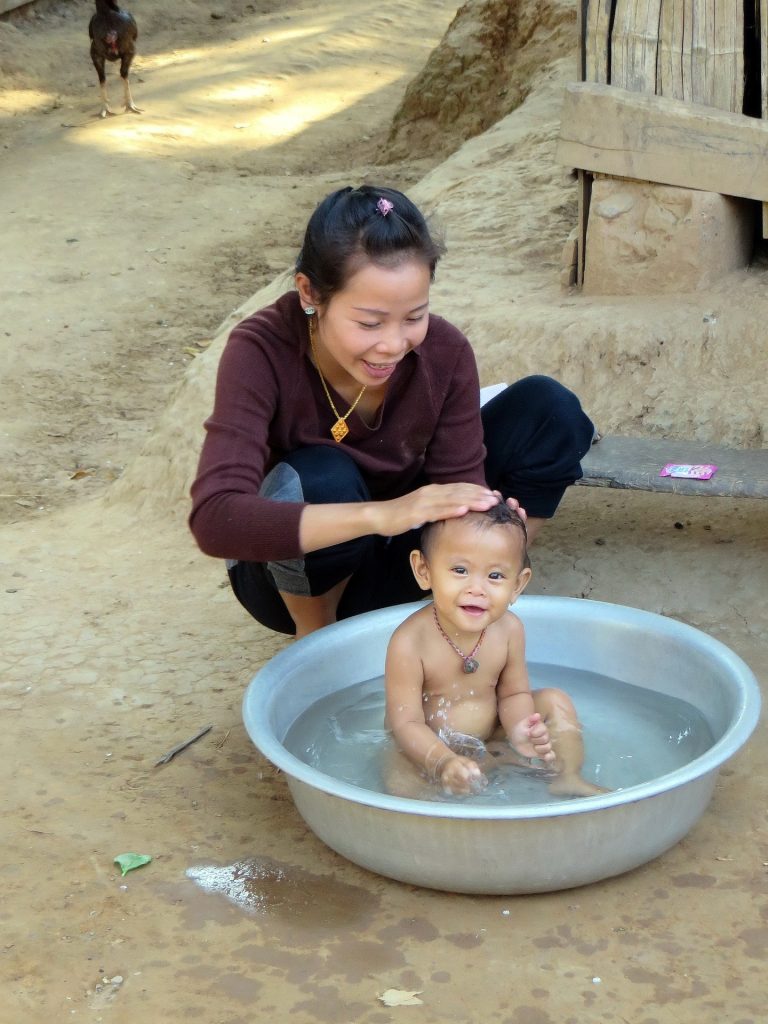 Woman bathing a smiling baby in a small outdoor basin in local community