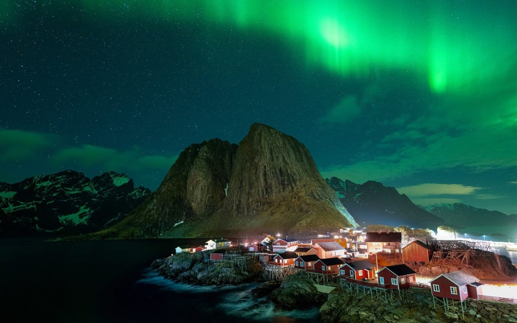 Green Northern Lights glowing above a coastal village and mountains in Norway
