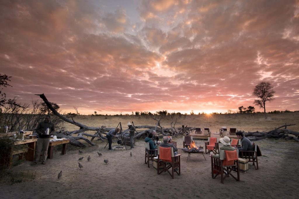 Travellers gathered around a campfire at sunset during an African safari