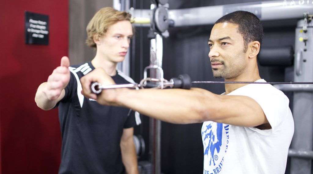 A personal trainer spots a man on an upper body weight machine.