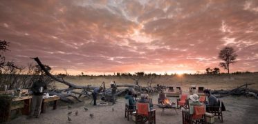 Travellers gathered around a campfire at sunset during an African safari